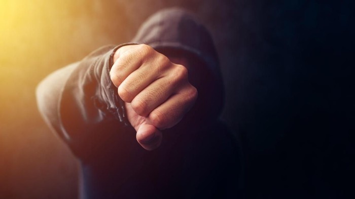 Crime, violence and bullying concept with hooded criminal person, selective focus on fist