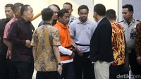 Dia tampak dikawal masuk ke mobil tahanan.