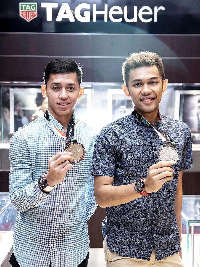 Begini gaya Fajar dan Rian memamerkan medali perak, berikut jam tangan TAG Heuer Carrera Heuer 01. Kemeja biru kotak-kotak menjadi pilihan Rian, sementara rekannya, Fajar, memilih kemeja abu-abu dan celana coklat. (Foto: dok. Time International)