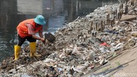 Seorang petugas mengeruk tanah dan membersihkan berbagai jenis sampah di pinggir Kali Grogol.