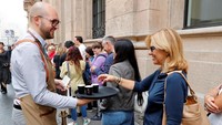 Seorang anggota staf Starbucks Reserve Roastery menawarkan kopi kepada pelanggan dalam antrean menunggu di pintu masuk, selama hari pembukaan di pusat kota Milan. Stefano Rellandini/Reuters.