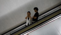 Seorang penumpang perempuan, bersama rekannya, bereaksi sambil kedua tangannya memegang pipi. Mereka sedang turun menggunakan eskalator stasiun bawah tanah di Pyongyang. Reuters/Danish Siddiqui.