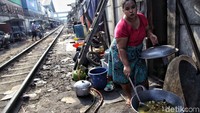 Seorang warga memasak di pinggir rel kereta api di kawasan Tanjung Priok, Jakarta Utara.
