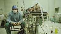Ahli bedah Zbigniew Religa usai menyelesaikan operasi transplantasi jantung selama 23 jam. Dirinya duduk dengan wajah cemas mengawasi tanda vital pasien sementara asistennya beristirahat di lantai. Foto: National Geographic