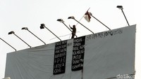 Dia memanjat baliho sambil mengibarkan bendera merah putih.