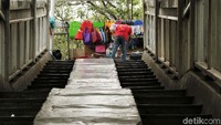 Seorang pedagang menggelar lapak tepat di depan tangga JPO.