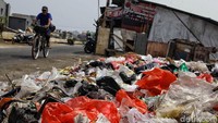 Seorang warga melintas di depan tumpukan sampah.
