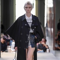 Referensi punk juga muncul pada look yang terdiri dari blus putih yang dibungkus terusan berbahan jaring serta rok kulit berkantong, lalu trench coat hitam sebagai luaran.  Trench coat sebagai produk signature Burberry juga mendapat sentuhan baru dengan siluet lengan yang lebih lebar. (Foto: Dok. Vogue)