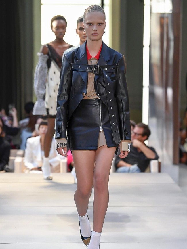 Rasa punk di koleksi terbaru Burberry terasa lewat kehadiran jaket bikers hitam berbahan kulit dengan sabuk di bagian dada. Jaket tersebut dipadukan dengan blus beige bergaya formal dengan rok kulit beraksen ritsleting di bagian depan. Di tangan Riccardo, kesan pemberontak yang selama identik dengan budaya punk berpadu apik dengan elegansi Burberry sebagai rumah mode yang eksis sejak 162 tahun itu. (Foto: Dok. Vogue)