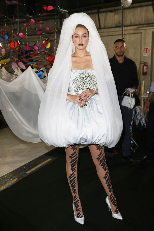 Gaunnya tampak unik dengan stocking putih berhias coretan hitam, bersama kerudung unik yang diselipkan ke bawah gaun dan mengalir di belakangnya. Foto: Dok. Getty Images