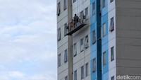 Dengan menggunakan gondola, petugas membersihkan jendela tiap lantai.