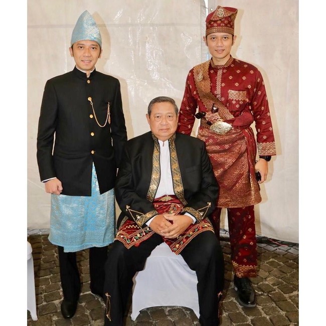 Baju tradisional Banjar khas Kalimantan Selatan menjadi andalan SBY, lengkap dengan topi dan kain adat bernuansa kemerahan.  Adapun kemeja hitam yang dipakai sebagai luaran dihiasi detail payet bernuansa emas pada bagian kerah dan manset. (Foto: Instagram/@aniyudhoyono)