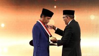 Pantauan detikFinance, Rosan mengalungkan penghargaan ke leher Jokowi di atas panggung. Penghargaan tersebut berupa kalung piagam dengan tali merah putih melambangkan bendera Indonesia.