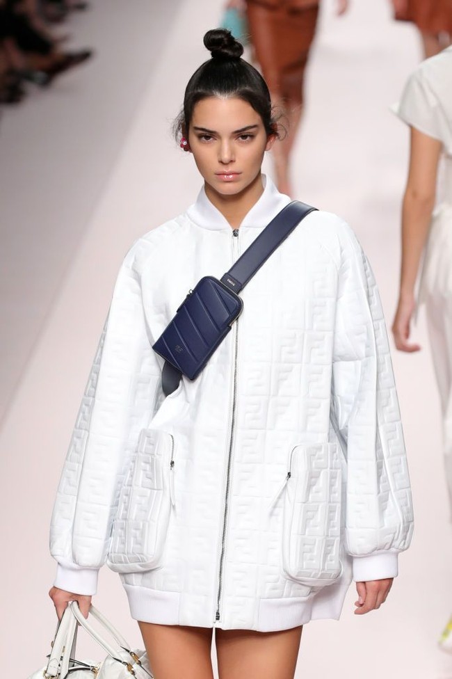 Gaya Kendall Jenner pakai baju tanpa celana terlihat kasual namun tetap glamor. Jaket oversized dipadukan dengan tas berwarna senada, sepatu kitten heels dan fanny pack biru navy. Foto: Getty Images