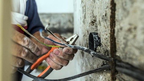 Photo of Electrician peeling off insulation from wires - closeup on hands and pliers. electrician binding copper wires together and sealing them with insulation stripe. Man mounting the wires into electrical wall fixture or socket - closeup on hands and pliers.