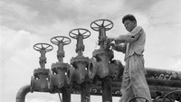 Seorang pekerja sedang mengoperasikan katup induk yang mengontrol jalur pipa di sebuah kilang minyak di Sumatera sekitar tahun 1955.  
