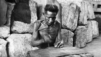 Seorang pekerja tampak menyusun tumpukan karet untuk dikirim ke Timur Portugis sekitar tahun 1950.  