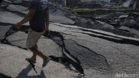Seorang warga melintas di jalan yang ambles akibat gempa.