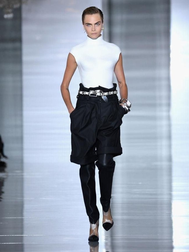 Cara lalu muncul lagi dengan look monokrom yang terdiri dari atasan turtleneck tanpa lengan serta celana pendek hitam yang dipadu dengan legging. Aksesori metalik yang bernuansa futuristik turut melengkapi gayanya. (Foto: Pascal Le Segretain/Getty Images)