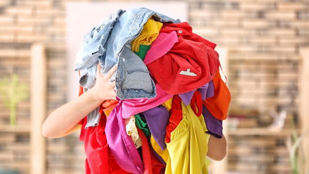 Woman holding pile of colorful clothes indoors