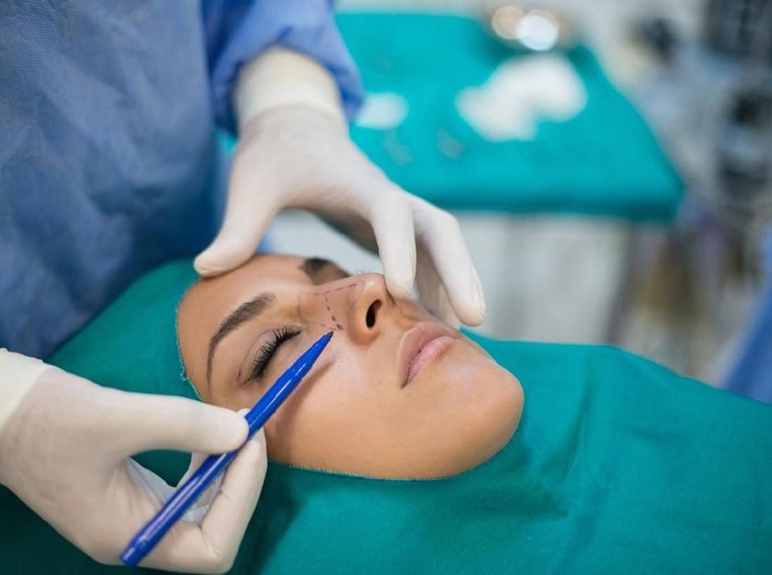 operasi plastik Close-up Of A Surgeon Drawing Perforation Lines On Young Womans Face For Plastic Surgery