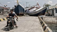 Warga melintas di depan kapal nelayan yang terbawa arus ke daratan.