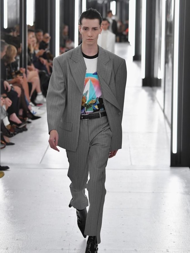 Dari Kanada, ada Krow yang juga terlahir sebagai perempuan. Di catwalk, ia diberi mandat memeragakan setelan berjas abu-abu dengan dalaman kaus bervisual grafis. (Foto: Pascal Le Segretain/Getty Images)