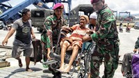 Dua prajurit TNI menggotong kursi roda yang dinaiki seorang ibu menuju pesawat Hercules.