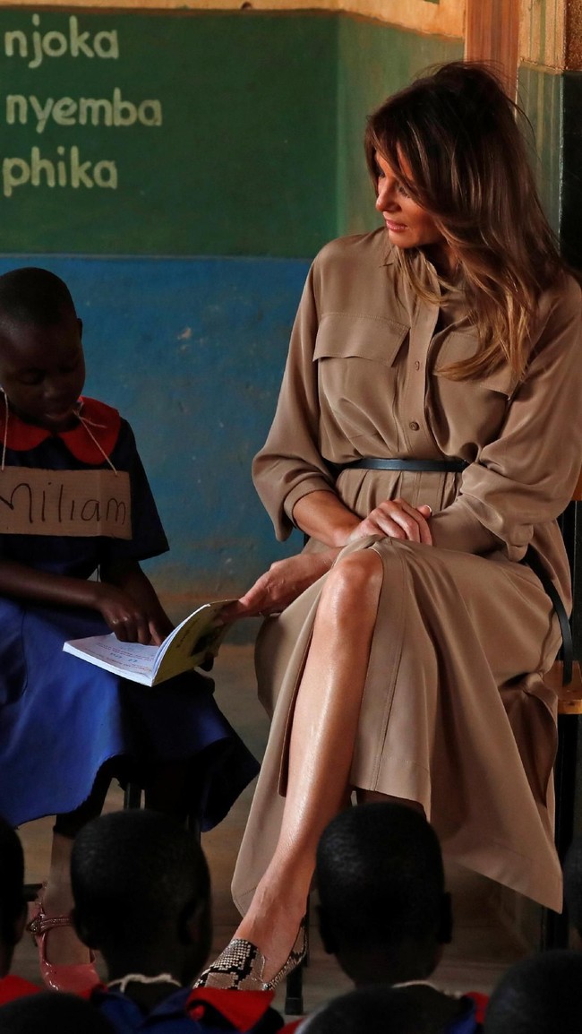Dari Ghana, tur Melania berlanjut ke Malawi di mana ia bertemu dengan murid-murid SD setempat. Shirt dress coklat bergaya safari dengan sabuk tali yang manis dan suede heels oranye Manolo Blahnik jadi andalan sang mantan model itu. (Foto: Reuters)