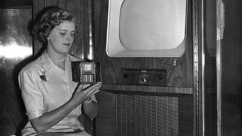 Jangan lihat TV di belakang, tapi perhatikan tangan si perempuan. Ya, di foto tahun 1951 ini, ia memegang TV 1 inci yang fungsional. (Foto: Topical Press Agency/Getty Images)