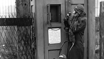 Dalam foto yang diambil tahun 1930 ini, seorang perempuan tampak menggunakan fasilitas telepon umum darurat yang otomatis menghubungkan dengan polisi. (Foto: Fox Photos/Getty Images)