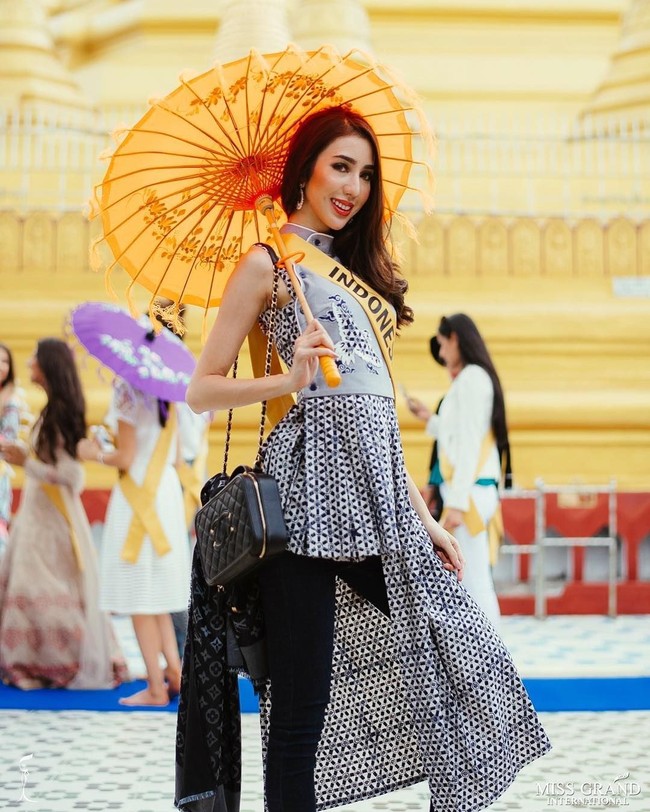 Nadia Purwoko tampak berpose cantik memakai dress asimetris motif batik kawung yang dipadukannya dengan celana hitam dan tas Chanel serta syal Louis Vuitton. Foto: Instagram Miss Grand Indonesia