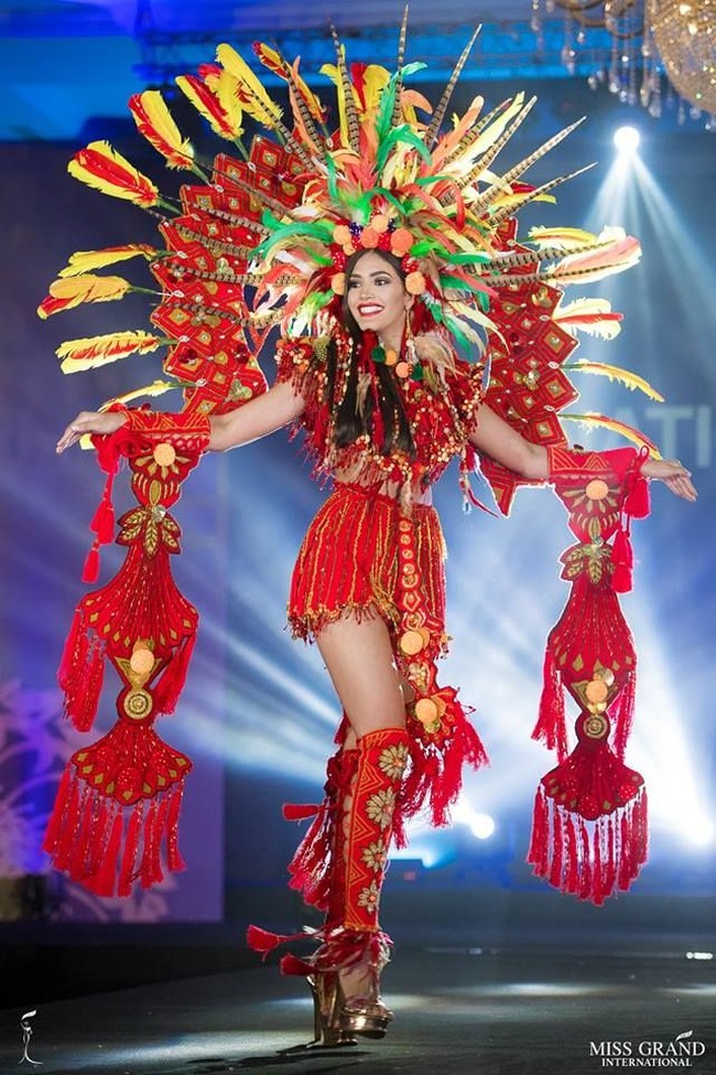 Miss Grand Venezuela Biliannis Alvarez yang difavoritkan menjadi juara Miss Grand International 2018 tampil heboh dengan kostum nasional serba merah. Dia memakai busana rumbai dan kepalanya dihiasi bulu-bulu. Pada kedua tangannya dia juga seperti membawa hiasan rumbai berwarna merah. Foto: Facebook Miss Grand International