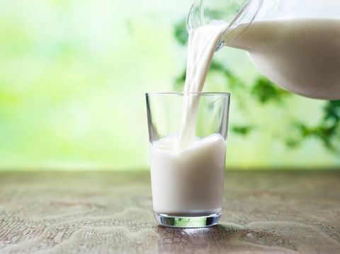 happy young woman drinking milk over grey background