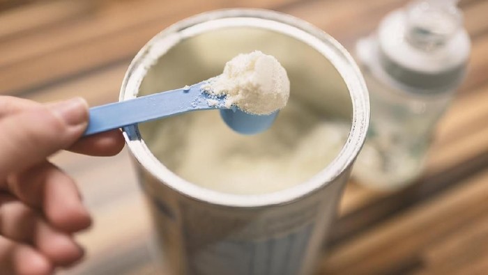 Powder milk for baby and blue spoon on light background close-up. Milk powder for baby in measuring spoon on can. Powdered milk with spoon for baby. Baby Milk Formula and Baby Bottles. Baby milk formula on kitchen background