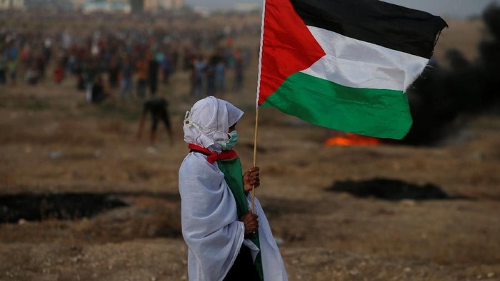 A woman holds a Palestinian flag during a protest calling for lifting the Israeli blockade on Gaza and demanding the right to return to their homeland, at the Israel-Gaza border fence in Gaza October 19, 2018. REUTERS/Mohammed Salem