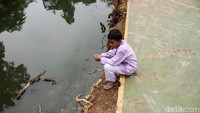 Seorang anak duduk termangu di pinggir sungai.