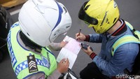 Seorang pemotor menandatangani surat tilang.