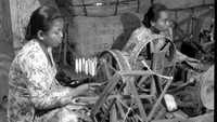 Dua orang wanita sedang bekerja di pabrik tekstil yang masih menggunakan peralatan manual pada tahun 1955. Three Lions/Getty Images.