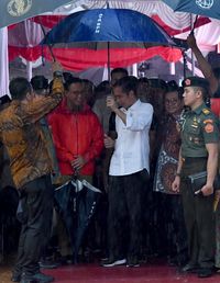 Anies terlihat memegang payung yang belum dibuka, sementara Jokowi sudah membuka payungnya. 