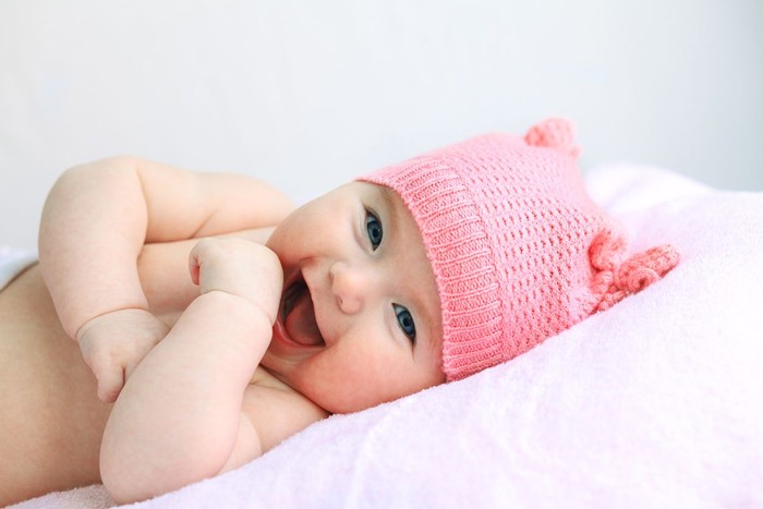 laughing european baby girl with big blue eyes in pink hat