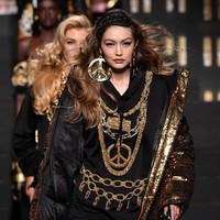Gigi Hadid muncul sebagai pembuka fashion show. Model 21 tahun ini tampil edgy dengan hoodie dress yang dipadu coat emas serta thigh-high boots. Tak lupa perhiasan statement yang sangat khas Moschino. (Foto: Getty Images)