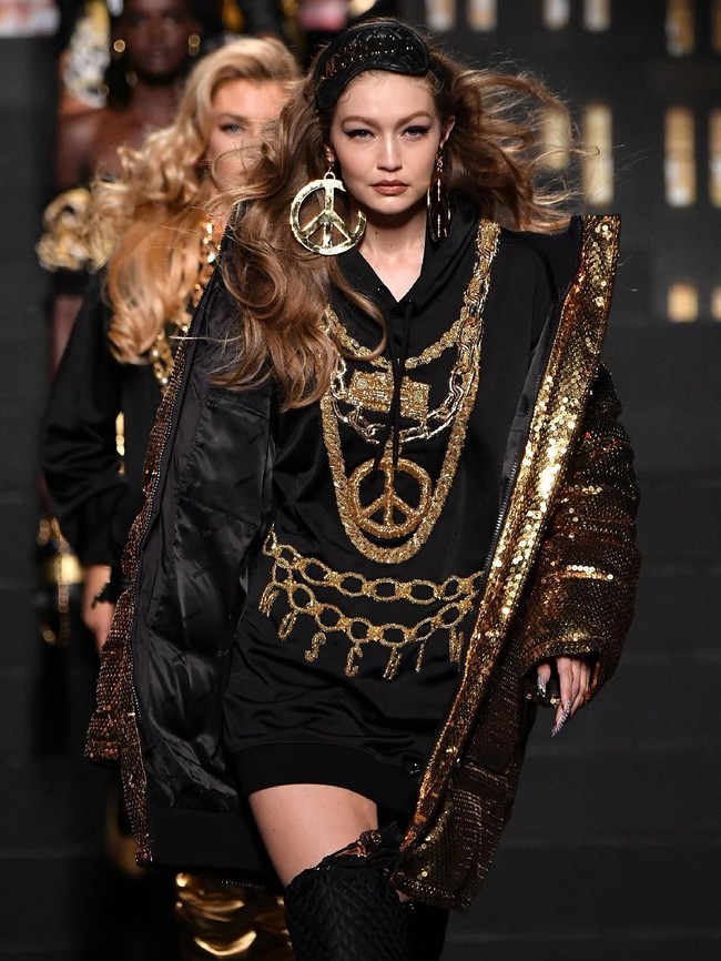 Gigi Hadid muncul sebagai pembuka fashion show. Model 21 tahun ini tampil edgy dengan hoodie dress yang dipadu coat emas serta thigh-high boots. Tak lupa perhiasan statement yang sangat khas Moschino. (Foto: Getty Images)