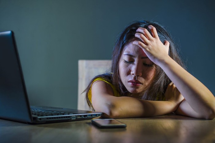 dramatic portrait scared and stressed Asian Korean teen girl or young woman with laptop computer and mobile phone suffering cyber bullying stalked and harassed with internet password hacked