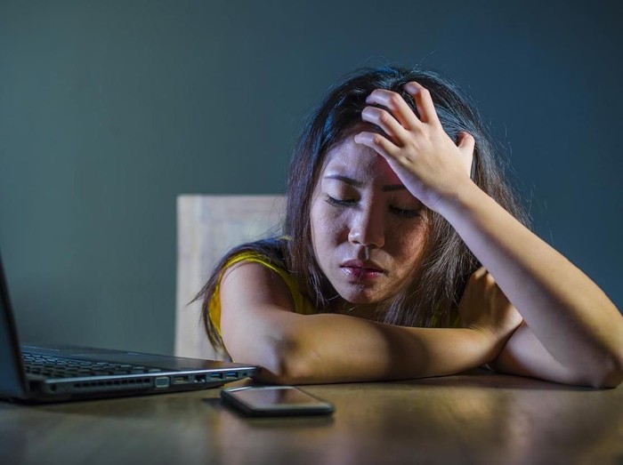 dramatic portrait scared and stressed Asian Korean teen girl or young woman with laptop computer and mobile phone suffering cyber bullying stalked and harassed with internet password hacked