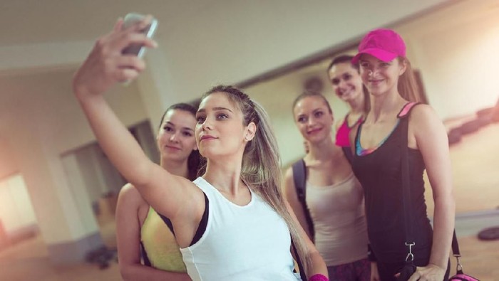 600396030 Healthy man prepare for next exercise in gym during hard cross training, while his friends having short rest and take a selfie. They wearing professional sport clothing .