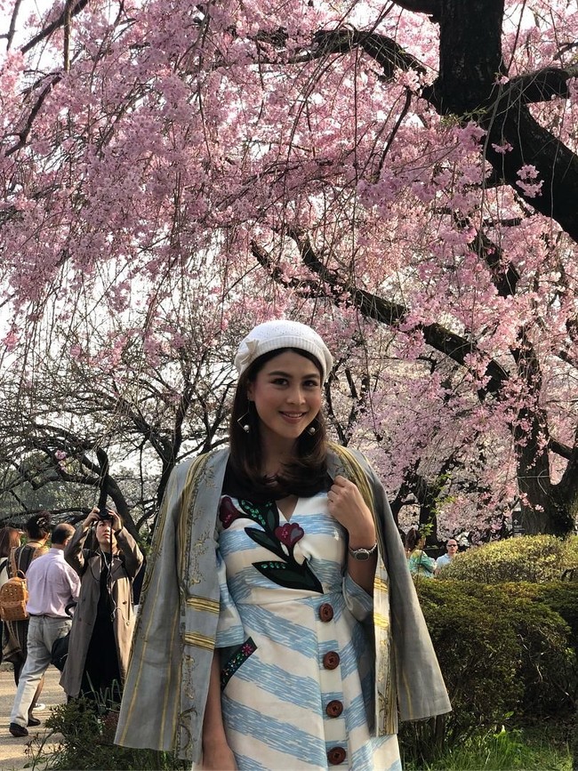 Nusara Suknamai berpose di bawah rindangnya pohon Sakura di Ueno Park, Tokyo, Jepang. Gaya busananya kekinian dengan dress bermotif embellishment floral dan blazer sebagai luaran. (Foto: Instagram/zara_nusara)