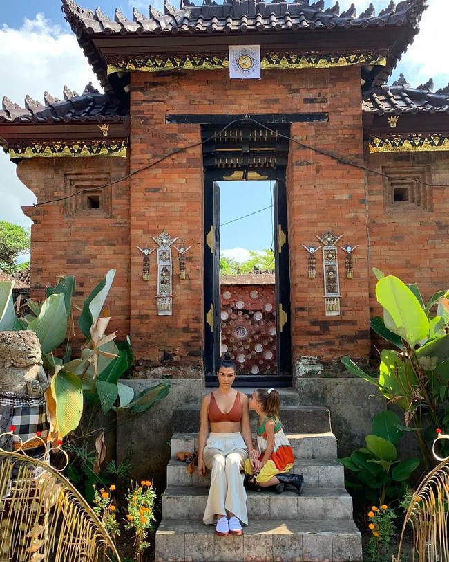 Udara Bali yang panas tampaknya membuat Kourtney merasa nyaman tampil dengan bralette atau crop top. Ketika berpose di depan bangunan khas Bali bersama sang putri, ia menggunakan bralette cokelat yang dipadukan dengan celana putih longgar serta sneakers. Foto: Instagram @kourtneykardash
