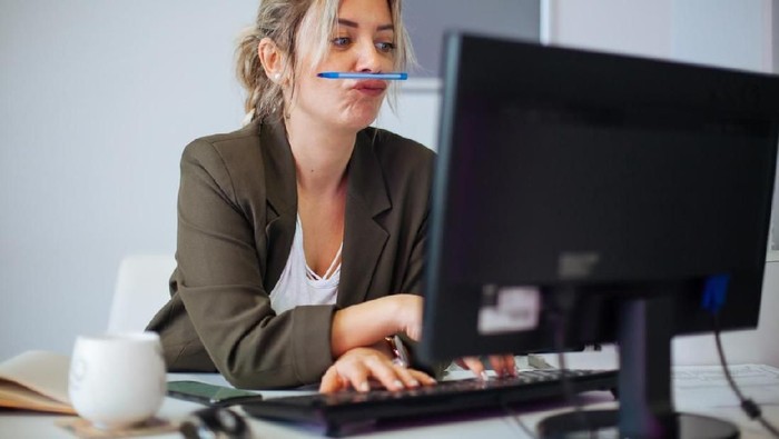 An exhausted customer service rep snoozing on her computer with her hand still clutched to her coffee.