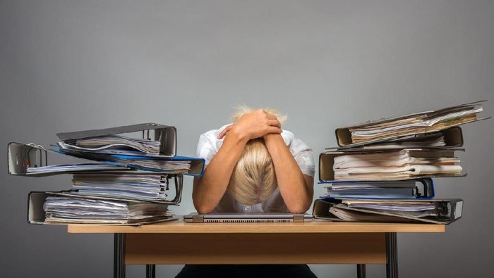 An exhausted customer service rep snoozing on her computer with her hand still clutched to her coffee.